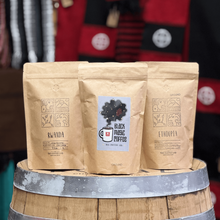 Load image into Gallery viewer, Three coffee bags stacked on a wooden barrel with a blurred background